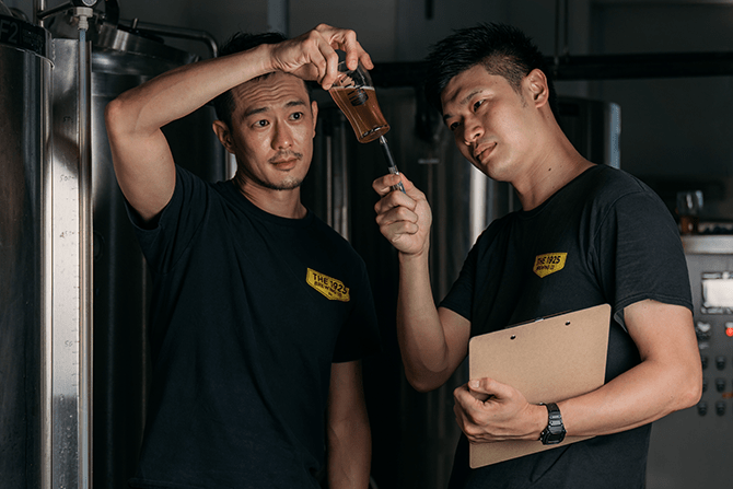 Ivan and E.K. Yeo examining a cup of beer in the brewery
