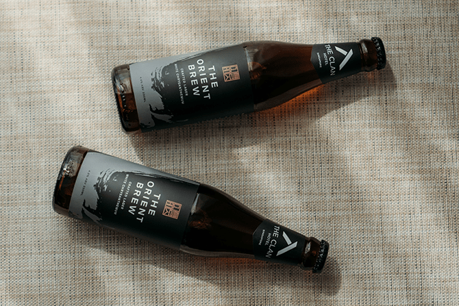 Two bottles of The Orient Brew laid down on a surfacel